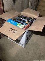 Box full of various paperback novels with titles visible on spines