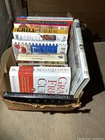 Top-down view of multiple cookbooks in a box, showing colorful spines and titles related to cooking and dietary health.
