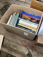 Box full of large books, mixed genres, showing titles and visible spines including sportfishing and royal family.
