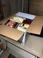 Box partially opened showing the spines and covers of several paperback novels inside the box.