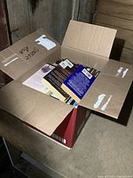 Open cardboard box filled with a variety of paperback novels stacked vertically and horizontally.