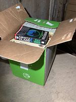 Box of novels and history books with one book clearly visible titled 'Nimitz Class' by Patrick Robinson on top of others inside a cardboard box.