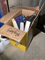 Box partially filled with nine novels, titles and authors partially visible on spines and covers.