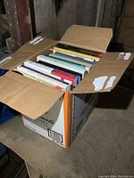 Box open showing spines of about thirteen books in various colors and sizes.