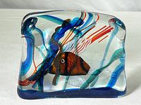 Front view of solid clear glass rectangular block with a hand-formed orange and black striped goldfish inside, surrounded by blue, red, and green swirls resembling aquatic plants.