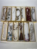Top-down view of all 14 costume jewelry necklaces laid out in individual gold paper gift boxes showing variety in bead types, colors, chain styles, and pendants.