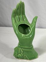 Green hand shaped ceramic vase shown from an angled side view, displaying glossy green glaze and base detail, highlighting the hand form and opening in palm.