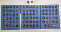 Full view of three blue Whitman coin holders showing multiple slots for Lincoln Head pennies from 1909 to 1940; many slots empty.