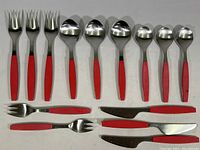 Overview of the full flatware set arranged on white surface showing multiple forks, spoons, knives, and small fork, all with cranberry pink handles.