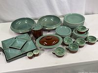 Full set of brown and green glazed pottery dinnerware including plates, bowls, cups, saucers, covered dishes, salt and pepper shakers, and condiment tray
