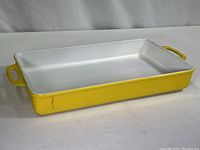 Side angle view of rectangular yellow enamel casserole dish on white surface.