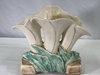 Side view of the ceramic vase shaped as three white lilies with green leaf bases on a brown ceramic support base.
