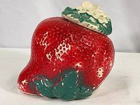 Front angle photo showing red strawberry shape with textured surface and green leaves at the base