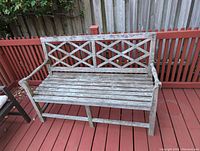 Front view of the weathered wooden bench showing slatted seat and crisscross backrest design.