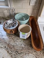 Photo of five decorative bowls and one long wooden boat-shaped bowl arranged on a kitchen counter.