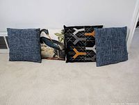 Four cushions arranged standing against a white wall, showing two blue/white cushions matching, one with a bird print, and one with geometric arrow pattern.