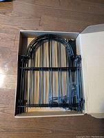 Photo showing ten black metal garden fence panels stacked inside a cardboard box, each panel having vertical bars and arched top design.
