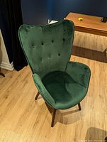 Front and side angle of the green wingback chair highlighting the tufted green velvet upholstery and wooden legs.