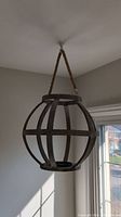 Wooden spherical globe hanging holder suspended by rope from ceiling, viewed from below and side in natural daylight.