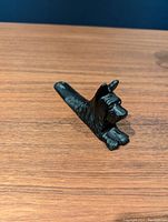 Black iron doorstop shaped like a small Scottie dog lying down, shown on a wood surface from a front angle