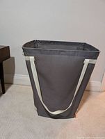 Front view of rectangular grey fabric laundry basket with white handles and wire frame for structure.
