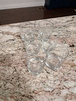 Six clear low ball glasses arranged on a speckled granite countertop.