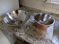 Two metal bowls on granite countertop, one large stainless steel bowl and one smaller copper finish hammered bowl