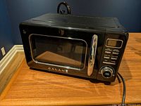 Front view of a black Galanz microwave oven with digital display and control buttons on the right side, including a chrome handle on the door.