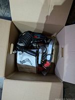Box containing a circular saw, drills, rotary tools, charger, and manuals as viewed from above showing tool arrangement and condition