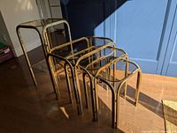 Photo showing four side tables, three nesting inside each other plus taller separate table, all with brass frames and glass tops.