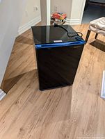 Front view of a small black Insignia mini fridge with a blue accent strip on the door, showing the closed fridge.