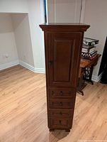 Front view of the tall wooden cabinet with a single cupboard door at the top and four drawers below.