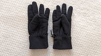 Pair of large black gloves laid flat on beige carpet showing front and back sides.