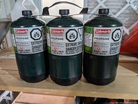 Photo showing three green Coleman propane cylinders for camping BBQs with safety warnings attached