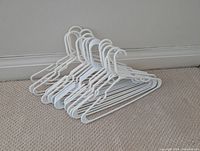 Twenty white plastic non-swivel clothes hangers stacked together on a floor against a wall.