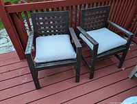 Front view of two dark wooden outdoor chairs with light cushions on a red wooden deck.