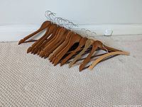 Sixteen wooden hangers arranged on a carpeted floor showing varying wood tones and metal hooks.