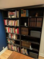 Two black IKEA bookshelves standing side by side against a wall, partially filled with books, boxes and small objects.