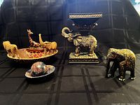 Photo showing five African and elephant themed decor items against a black background, including carved wooden bowl with animals, painted elephant figurine, Kashmiri elephant stand, soapstone ball and bowl.