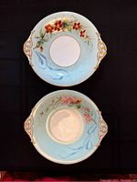 Two antique Victorian cake plates, round with side handles, light blue background, hand-painted floral design and gilt edges and handle decoration.