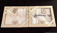 Two boxed Armani Baby blankets, one with pink and one with blue logos visible through the windowed boxes, tied with cream ribbons