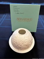 View of the Bernardaud Limoges branded box with the white porcelain votive globe on top, showing embossed Nativity scene detail.