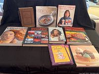 All nine books displayed on a black cloth background, variety of topics including cookbooks and art.