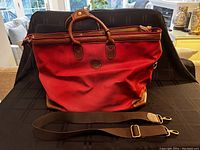 Front view of red canvas bag with top handles and detached shoulder strap laid in front