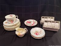 Full lot including tea cup, saucers, dessert plates, creamer, ashtrays, and porcelain napkin rings all displayed on black cloth background