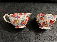 Two bone china pieces: creamer with handle and sugar bowl without handle, both decorated with colorful floral Marina pattern and visible light crackle glaze texture.