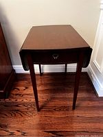 Side view of the wooden dropleaf side table showing the drawer and legs.