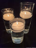 Three clear glass cylinder vases filled with water and floating white candles, viewed from above and front. All appear clean with no chips or cracks visible.