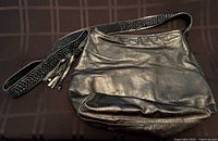 Handmade black leather shoulder bag laid flat on a brown surface showing its full body and beaded strap with tassel.