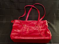Front view of the large red leather handbag with two shoulder straps on a black surface.